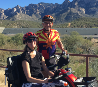 Claire Szabo (on mobility scooter) and Lou Cassella standing outdoors with desert mountains in background