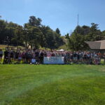 A large group of people gathered around and behind a "2025 Michigan Walk & Roll to Cure FSHD" banner