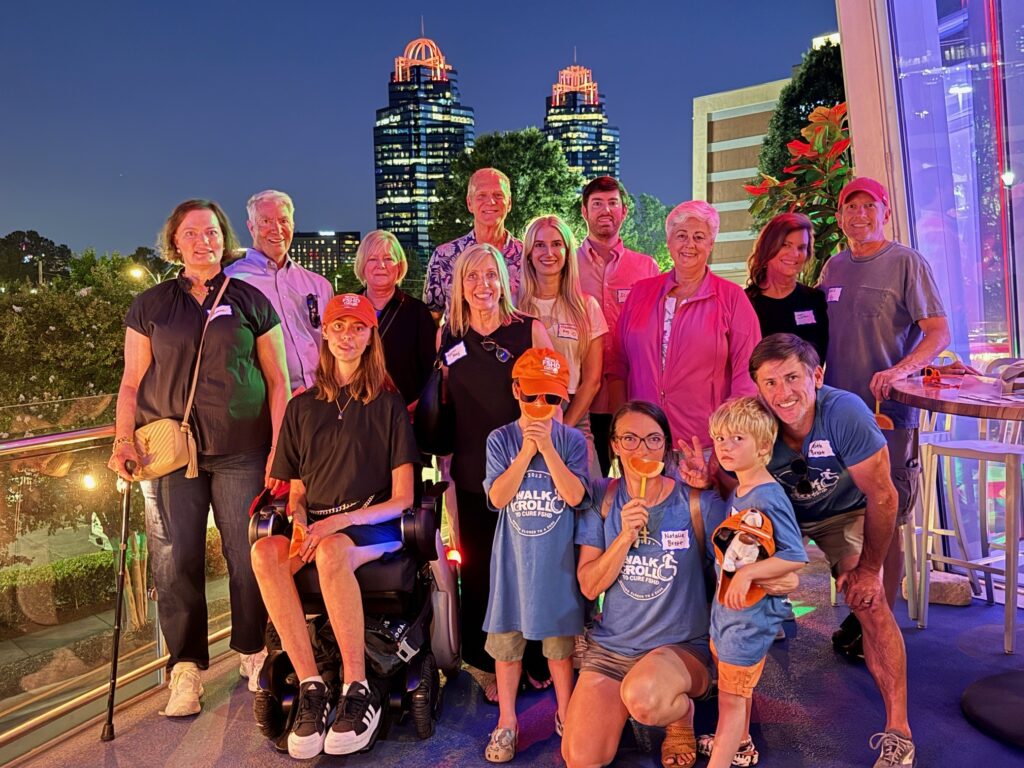 Multiple members of the Atlanta Chapter stand and sit in front of the King & Queen Towers, which are lit in orange. They hold orange slices in front of their mouths.