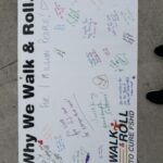 A large white banner with "Why We Walk & Roll" printed on it covered in reasons from event participants. These reasons are written in colorful markers.
