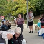 A young woman in a red shirt speaks into a microphone at an event.