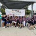 A group of people in red shirts stand in front of the 2025 Walk & Roll banner