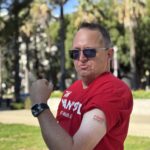 A Sacramento Walk & Roll participant in a red shirt flexes their bicep and shows off an FSHD Society temporary tattoo.