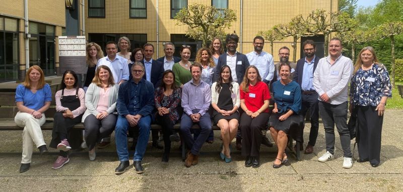 Group of scientist, researchers, and clinicians smiling at the camera during a conference. The photo was taken outside, in the sun, infront of an academic building.