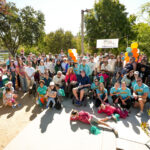 Group photo of participants at the 2026 Bay Area Walk & Roll to Cure FSHD. They look towards the camera with hopeful and happy expressions on their faces. They are in a park with trees and a sunny sky behind them