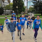 Members of Team Ryan's Hope walk toward the camera with joyful expressions on their faces. They are participating in the 2026 Sacramento Walk & Roll to Cure FSHD. They wear bright blue t-shirts with their team name in white and orange.